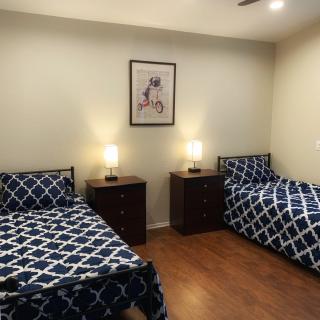 A tidy bedroom featuring two twin beds with matching patterned bedspreads, two nightstands each topped with a lamp, and a piece of wall art on a light-colored wall.