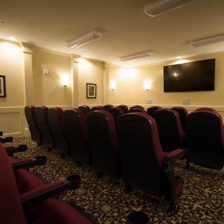An indoor theater room with rows of comfortable seating and a large screen on the wall.