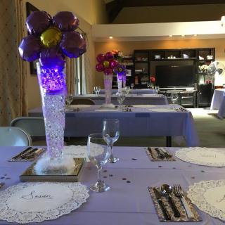 A festive table setting with purple-themed decorations and balloon centerpieces, ready for a celebration.