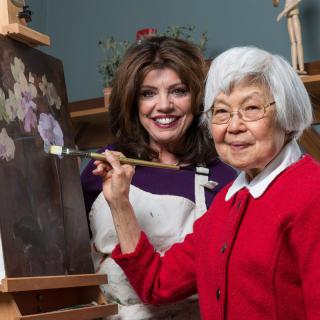 Two women enjoying a painting session together, with one of them holding a paintbrush in front of a canvas.