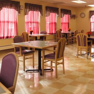 A cozy dining area featuring wooden tables, chairs with purple upholstery, and bright red curtains filtering natural light.