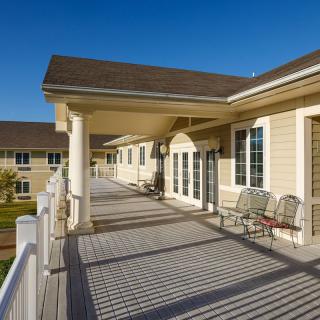 A spacious veranda with chairs, part of a modern building under a clear blue sky.