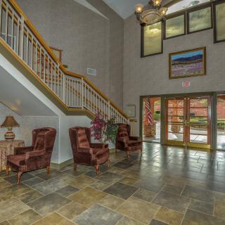A spacious lobby area with tiled flooring, featuring armchairs, a staircase, and large glass doors.
