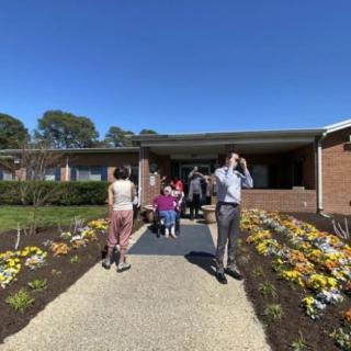 A group of people walking along a pathway lined with colorful flowers on a sunny day.