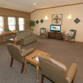 A cozy living room with comfortable seating and a television, featuring large windows and decorative artwork.