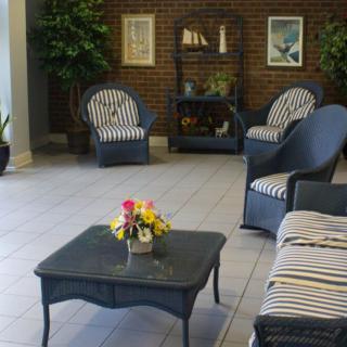 A cozy indoor lounge area featuring wicker furniture with striped cushions and a coffee table adorned with a floral centerpiece.