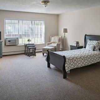 A spacious bedroom with a single bed, chair, and large window letting in natural light.