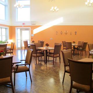 A modern dining area with tables and chairs, illuminated by natural light from large windows.