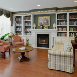 A cozy living room with a fireplace, surrounded by bookshelves and comfortable seating.