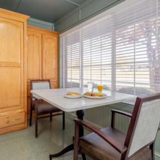 A cozy kitchen nook featuring a table set for breakfast with two chairs and a large window with blinds.