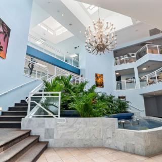 A modern interior space with a central staircase, lush plants, and a striking chandelier under natural light.