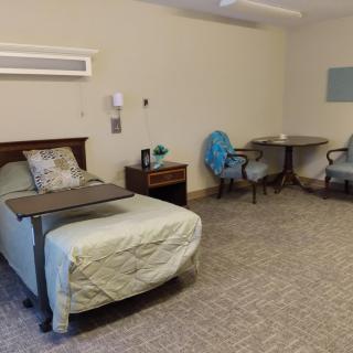 A hospital room with beds, tables, and chairs, featuring a simple and clean design.