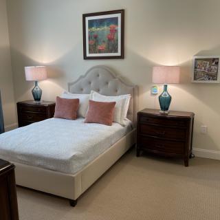 A cozy bedroom with a neatly made bed, flanked by two nightstands and lamps, featuring artwork on the wall.