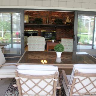 A cozy patio area with a wooden dining table and cushioned chairs, overlooking an indoor space through sliding glass doors.