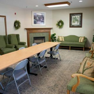 A conference room with a long table, multiple chairs, green seating, and decorative plants.