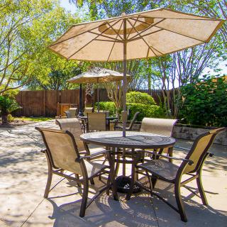 A sunny outdoor patio with a table, chairs, and umbrellas set among greenery.