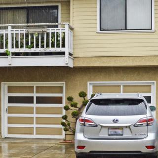 A silver car parked in front of a garage attached to a two-story house with a balcony.