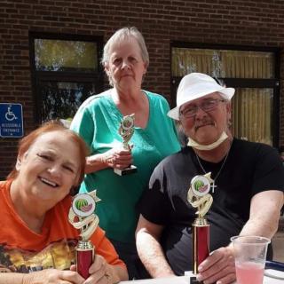 A group of three people holding trophies at an outdoor event.