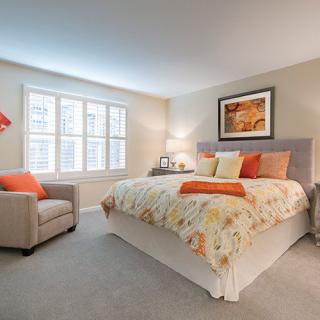 A cozy and modern bedroom featuring a neatly made bed with colorful pillows, an armchair, and artwork on the wall.