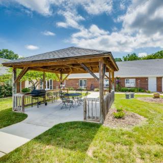 A cozy outdoor gazebo with patio furniture, set in a landscaped garden under a blue sky.