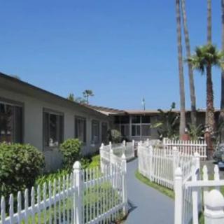 A sunny outdoor scene featuring a building with a white fence, palm trees, and a clear blue sky.