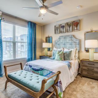 A cozy and stylish bedroom with blue accents, featuring a neatly made bed, elegant furniture, and plenty of natural light.
