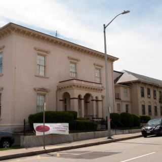 A historic building with classical architecture alongside a street containing a parked vehicle and a banner.