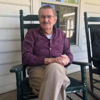 An elderly man sitting on a porch in a rocking chair.