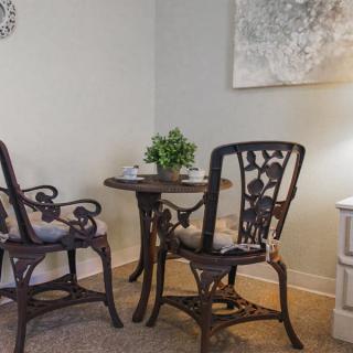A cozy dining area with a small round table and two ornate chairs, complemented by a potted plant and wall decor.