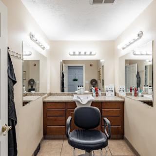 A well-lit bathroom area featuring a barber chair, multiple mirrors, and various hair care products.
