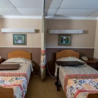 A hospital room with two beds separated by a curtain, each equipped with bedside tables and wall-mounted lights.