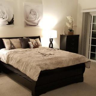 A cozy bedroom with elegant decor, featuring a large bed, stylish artwork, and a lamp on a bedside table.