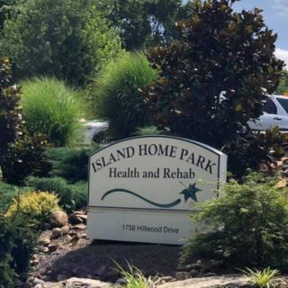 A sign for Island Home Park Health and Rehab surrounded by lush landscaping.