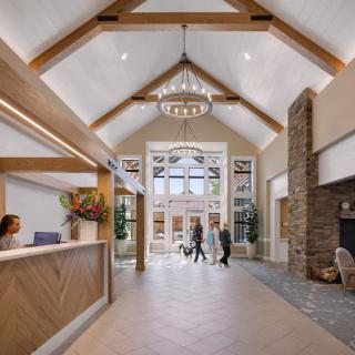 A modern lobby with a vaulted ceiling and chandelier, featuring a reception desk and large entrance doors.