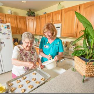 A caregiver assists an elderly woman in baking cookies in a cozy kitchen.