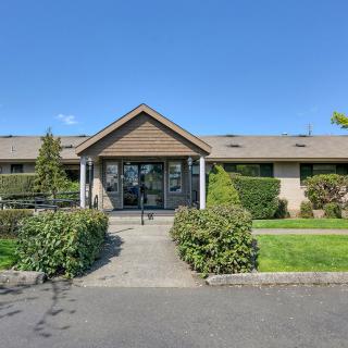 A building with a wooden entrance surrounded by well-maintained greenery and a clear pathway.
