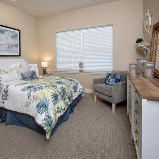 A cozy bedroom with a floral bedspread, featuring a wooden dresser and a comfortable armchair.