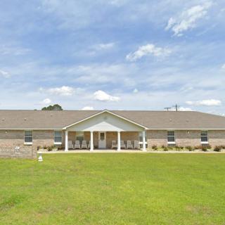 A single-story residential house with a large front lawn under a blue sky.