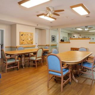 A spacious dining area with wooden tables and blue cushioned chairs, featuring wood flooring and ceiling fans.