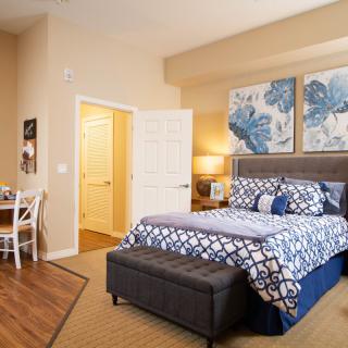 A cozy bedroom featuring a neatly made bed with blue and white patterned bedding, complemented by artwork on the walls.