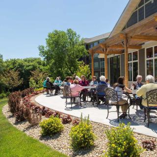 A group of people enjoying a sunny day on a patio with garden views.