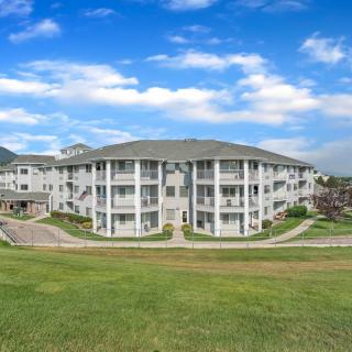 A modern residential apartment building surrounded by well-maintained landscaping under a partly cloudy sky.