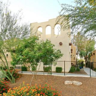 A desert-style building with arched windows, surrounded by trees and a landscaped garden.