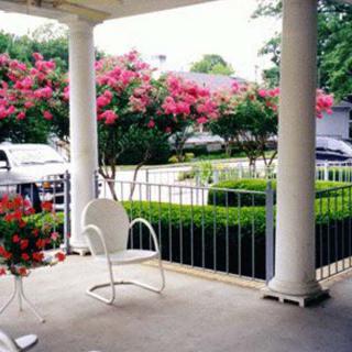 A cozy porch with white chairs and blooming flowers in a garden setting.