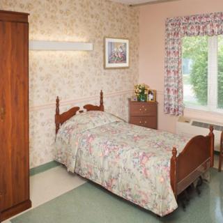 A cozy bedroom featuring a single bed with floral bedding, a wooden wardrobe, and a window with curtains.