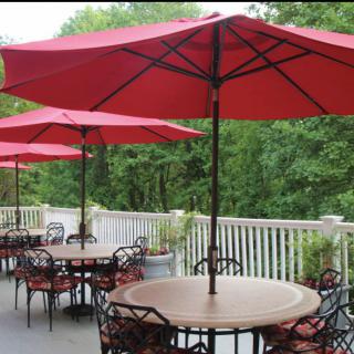 An inviting outdoor patio with red umbrellas and metal tables set against a lush, green backdrop.