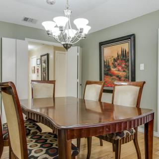 A dining room with a wooden table, upholstered chairs, a chandelier, and wall art.