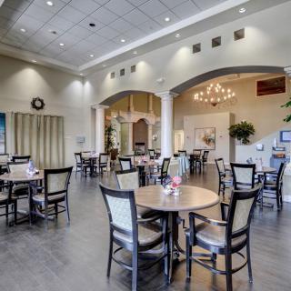 A spacious and elegantly decorated dining area with multiple tables and chairs, illuminated by a chandelier.