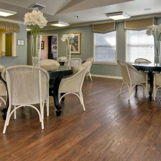 A dining area with wicker chairs and dark tables set on a polished wood floor.