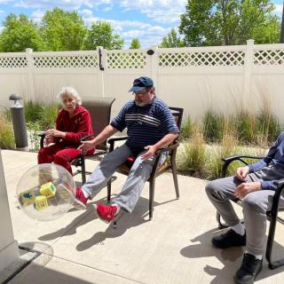 A group of people sitting outdoors near a white fence, enjoying a sunny day.